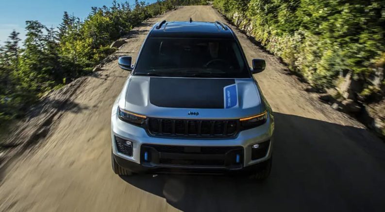 A grey 2023 Jeep Grand Cherokee 4xe is shown from the front driving on a dirt road.