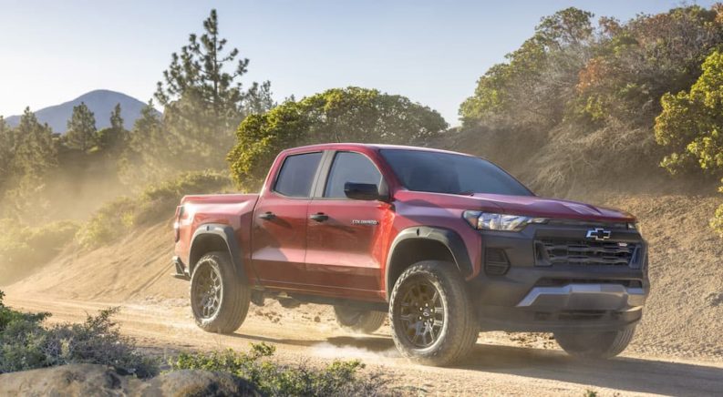 A red 2023 Chevy Colorado Trail Boss is shown from the front at an angle while driving off-road.