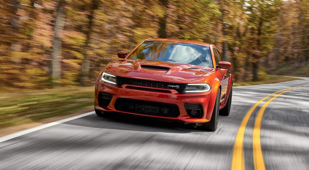 An orange 2022 Dodge Charger Hellcat is shown driving on an open road.