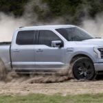 A silver 2022 Ford F-150 Lightning is shown from the side while driving off-road after leaving a dealer that advertised having a F-150 Lightning for sale.