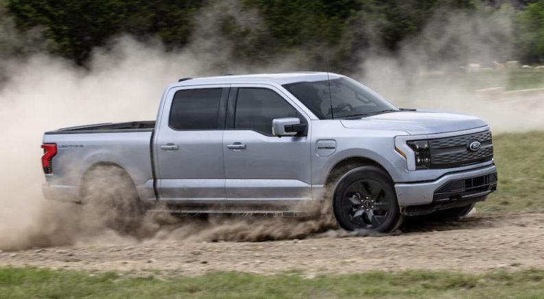 A silver 2022 Ford F-150 Lightning is shown from the side while driving off-road after leaving a dealer that advertised having a F-150 Lightning for sale.