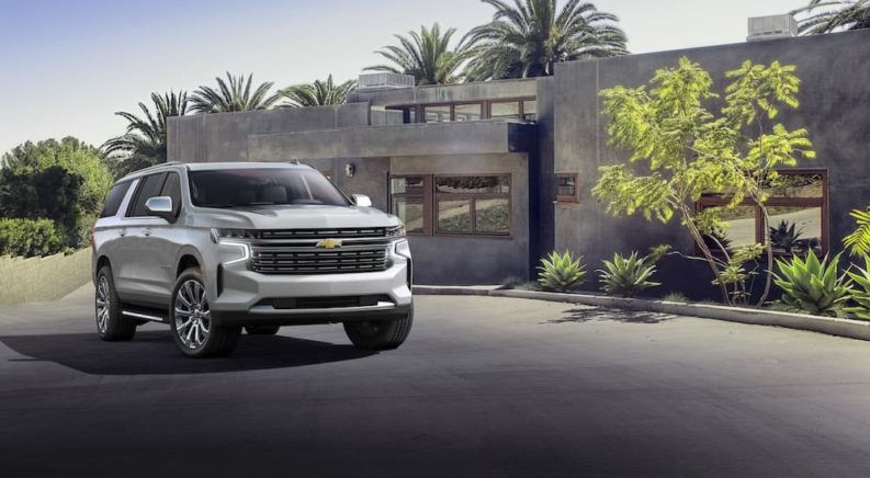 A silver 2021 Chevy Suburban is shown parked outside a modern house.