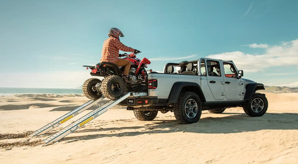 A white 2021 Jeep Gladiator is shown from the rear at an angle while being loaded with an ATV.