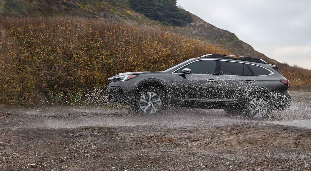 A grey 2022 Subaru Outback is shown from the side while driving through mud.