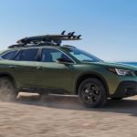 A green 2023 Subaru Outback is shown from the side while driving on a beach.