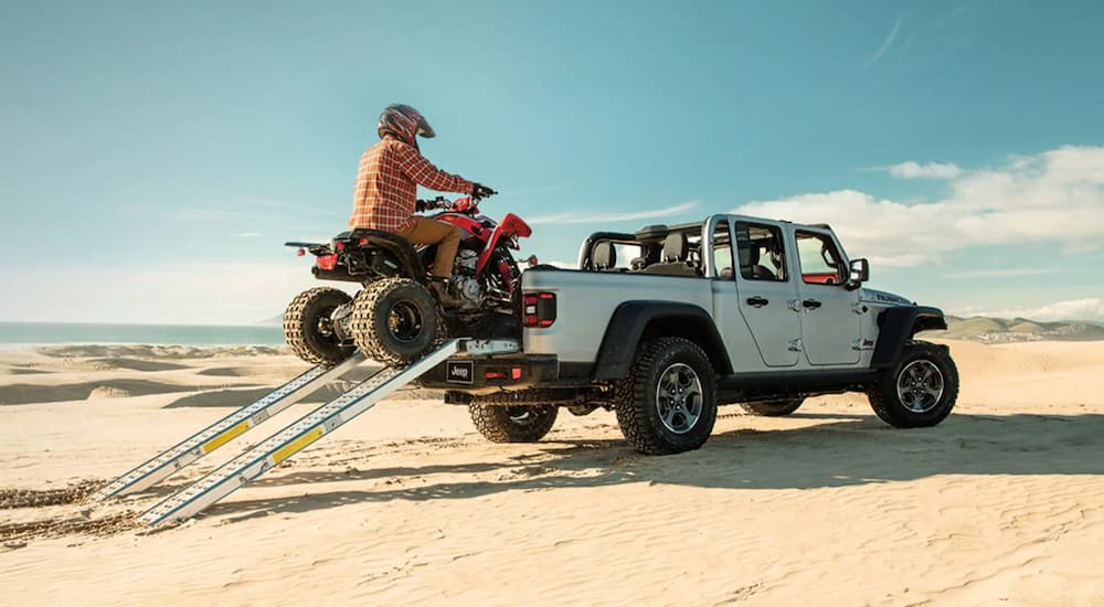 A person is shown driving an ATV into the bed of a white 2023 Jeep Gladiator.