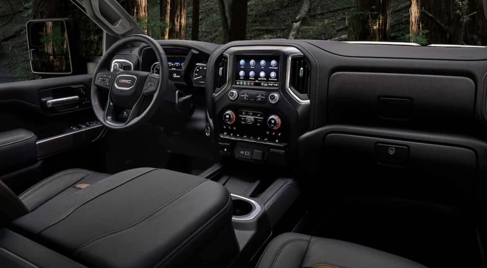 The black interior of a 2023 GMC Sierra 2500 HD AT4 shows the steering wheel and infotainment screen.
