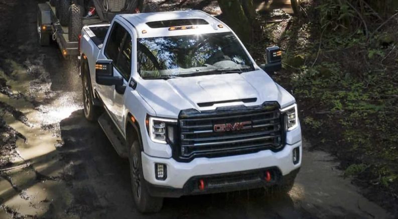 A white 2023 GMC Sierra 2500 HD AT4 is shown driving through the woods.