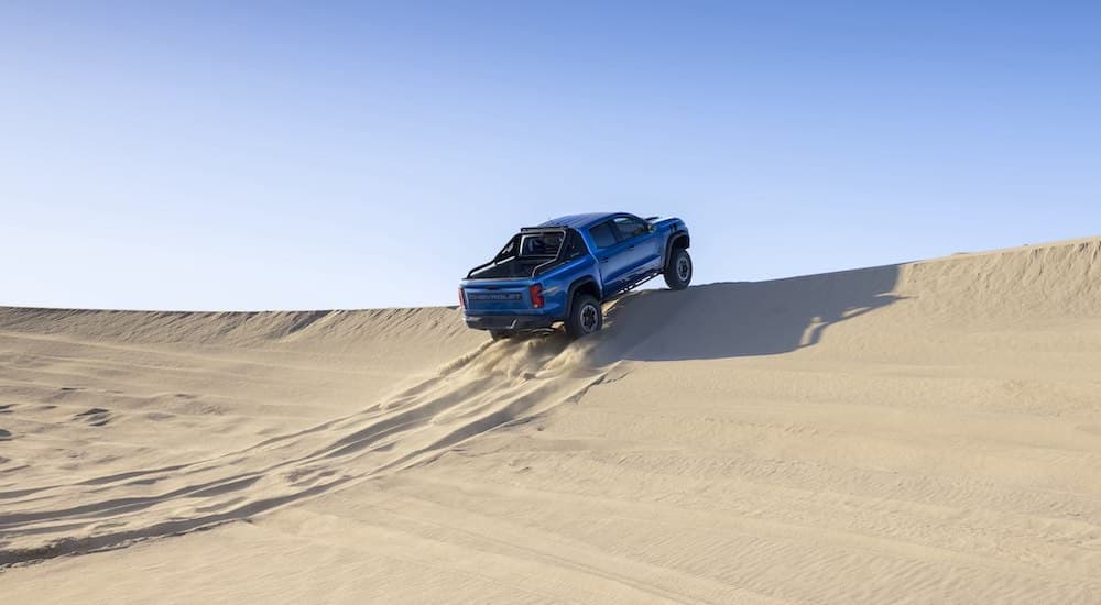 A blue 2023 Chevy Colorado ZR2 is shown from the rear while jumping off of a sand dune.