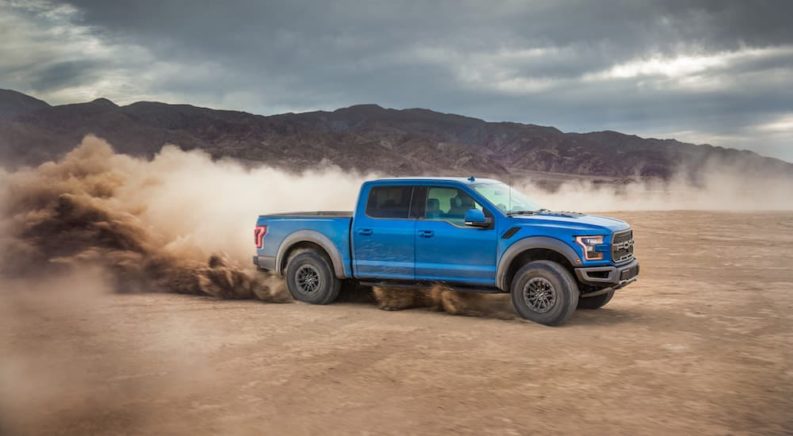A blue 2020 Ford F-150 is shown from the side kicking up dust on the way to a Ford F-150 dealer.