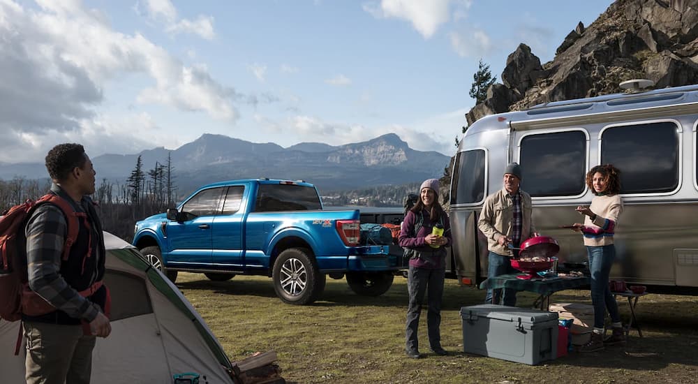 A blue 2022 Ford F-150 STX is shown towing a camper trailer.