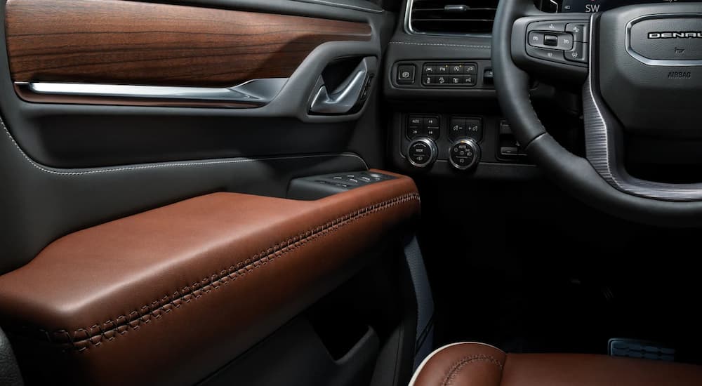 The brown and black interior fo a 2022 GMC Yukon Denali Ultimate shows the driver's side door and steering wheel.