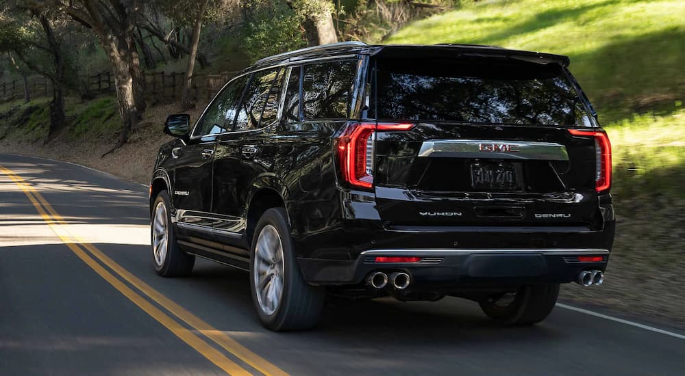 A black 2023 GMC Yukon Denali Ultimate is shown from a rear angle driving on a shady road.