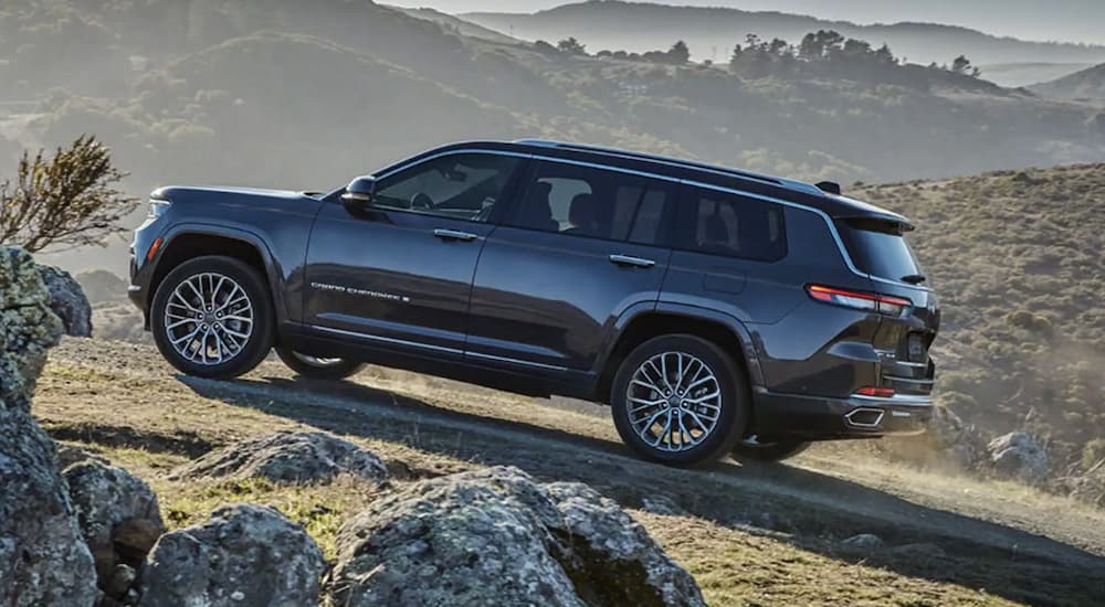 A black 2022 Jeep Grand Cherokee Trailhawk is shown from the side driving on a grass hill after leaving a Jeep Grand Cherokee dealer.