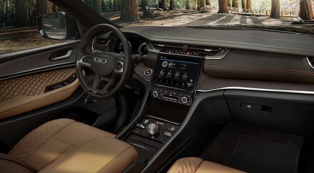 The black and tan interior of a 2022 Jeep Grand Cherokee Trailhawk shows the steering wheel and infotainment screen.