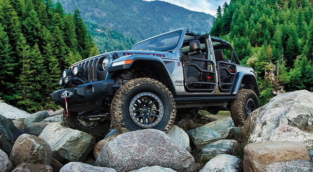 A grey 2021 Jeep Wrangler Rubicon for sale is shown driving over rocks. 