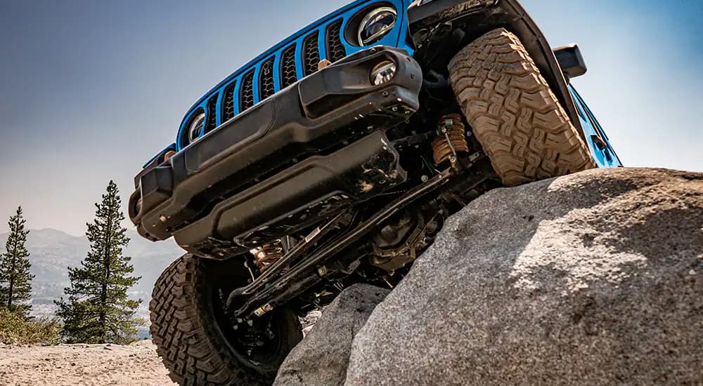 A blue 2022 Jeep Wrangler is shown driving over a large rock.