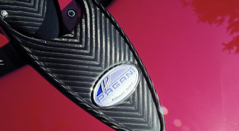 A close up of the logo and carbon on a red Pagani vehicle is shown.
