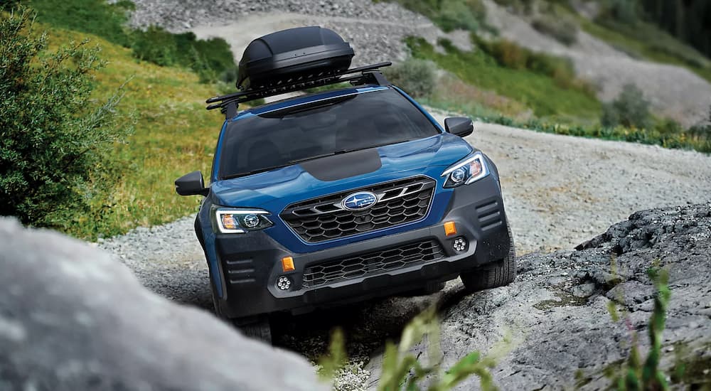 A blue 2023 Subaru Outback Wilderness is shown from the front on a steep rocky trail.