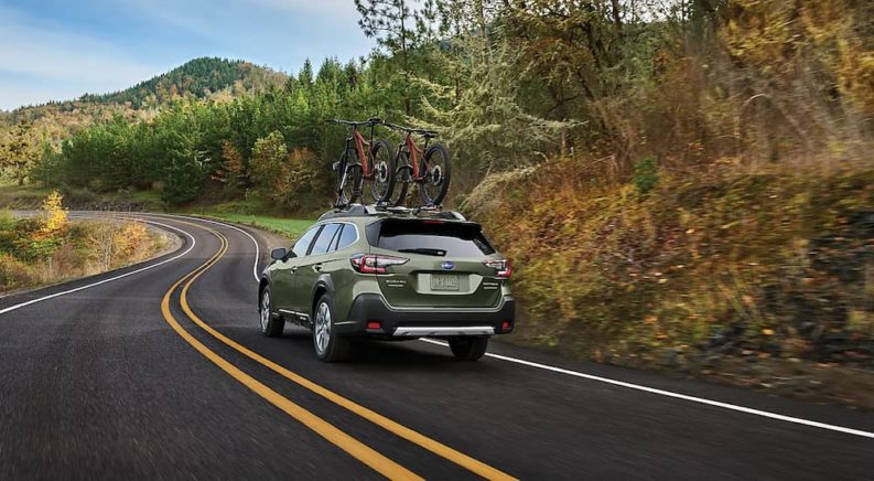 A green 2023 Subaru Outback is shown from a rear angle driving on a winding road.