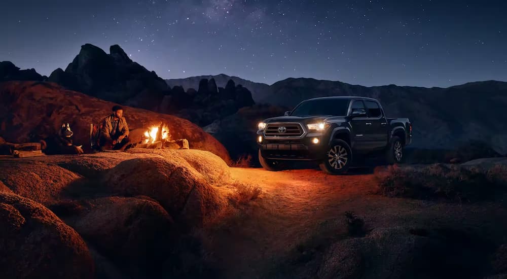 A black 2023 Toyota Tacoma SR5 is shown at a campsite at night.
