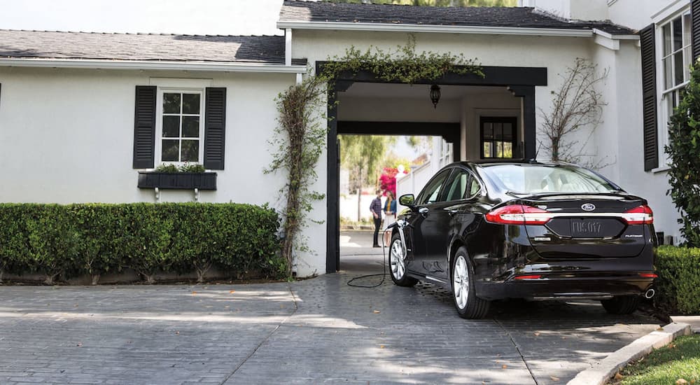 One of the most popular used cars for sale near you, a black 2020 Ford Fusion Hybrid Titanium, is show charging in a driveway. 