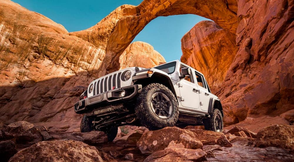 A white 2020 Jeep Wrangler Rubicon is shown from the front while driving over a rock.