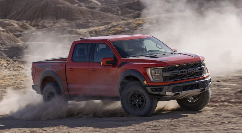 An orange 2022 Ford F-150 Raptor is shown from the side while sliding off-road after leaving a Ford F-150 dealer.