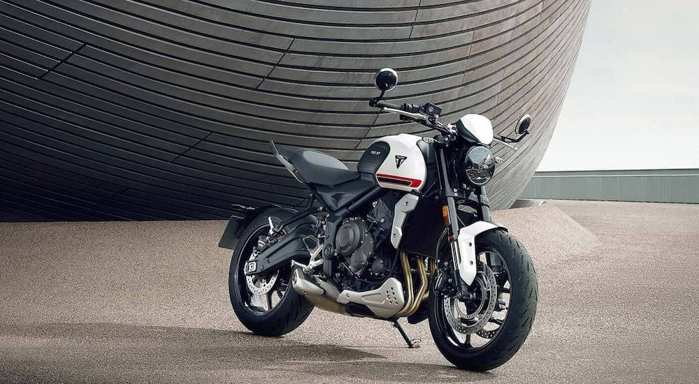 A white 2022 Triumph Trident 660 is shown parked in front of a modern structure.