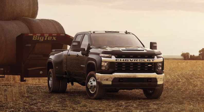A black 2023 Chevy Silverado 3500 HD is shown parked in a field towing a trailer.