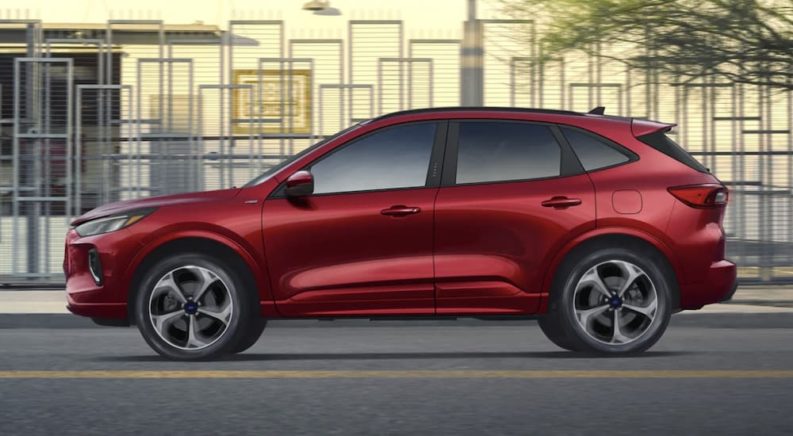 A red 2023 Ford Escape ST is shown from the side driving through a city.