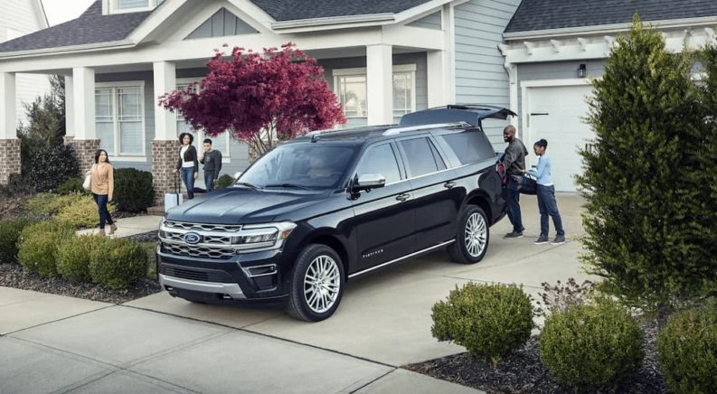 A black 2023 Ford Expedition Platinum is shown parked in a driveway as a family loads up cargo.