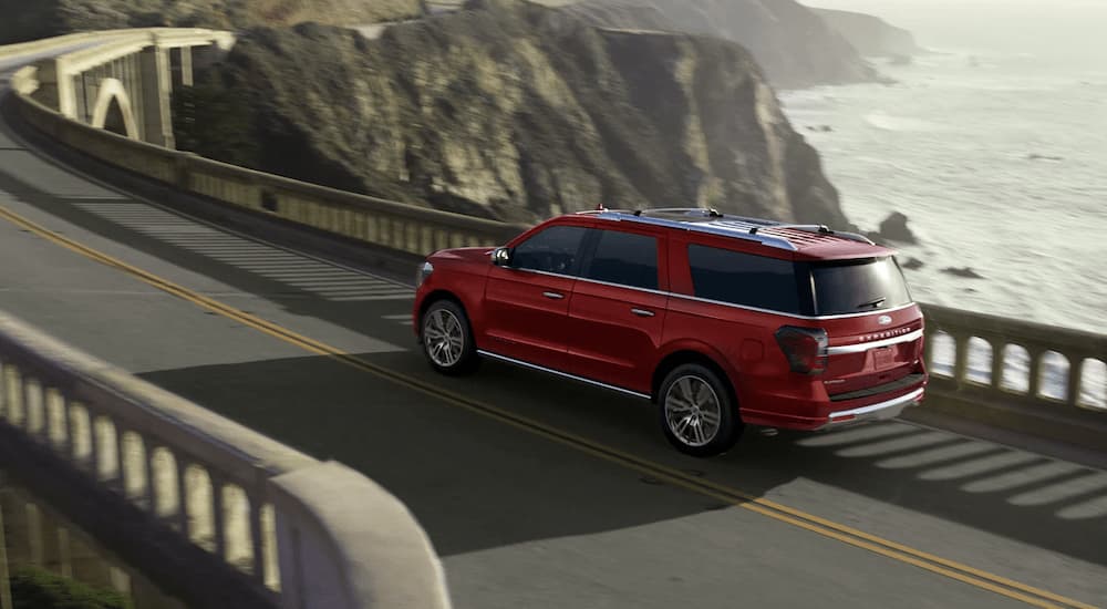 A red 2023 Ford Expedition Platinum is shown from a rear angle next to the ocean.