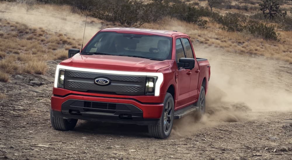 A red 2023 Ford F-150 Lightning is shown driving on a dirt road.