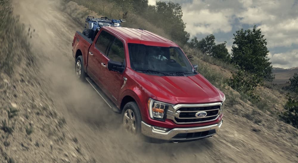 A red 2023 Ford F-150 is shown driving down a dirt road.