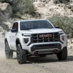 A white 2023 GMC Canyon AT4 is shown driving on a dirt road.