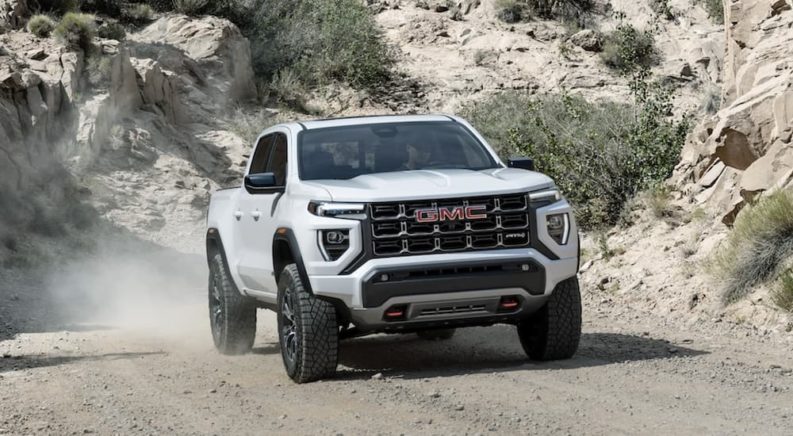 A white 2023 GMC Canyon AT4 is shown driving on a dirt road.