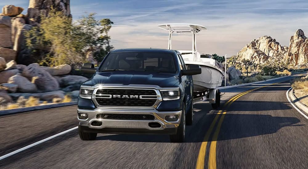 A blue 2023 Ram 1500 is shown towing a boat on an open road.