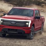 A red 2022 Ford F-150 Lightning is shown driving on a dirt road.