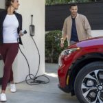 A couple is shown charging their red 2023 Ford Mustang Mach-E outside of their garage.