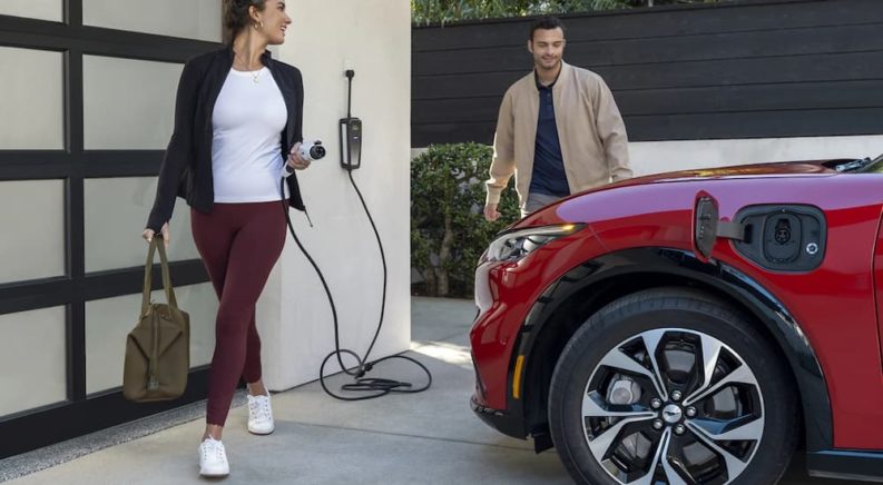 A couple is shown charging their red 2023 Ford Mustang Mach-E outside of their garage.