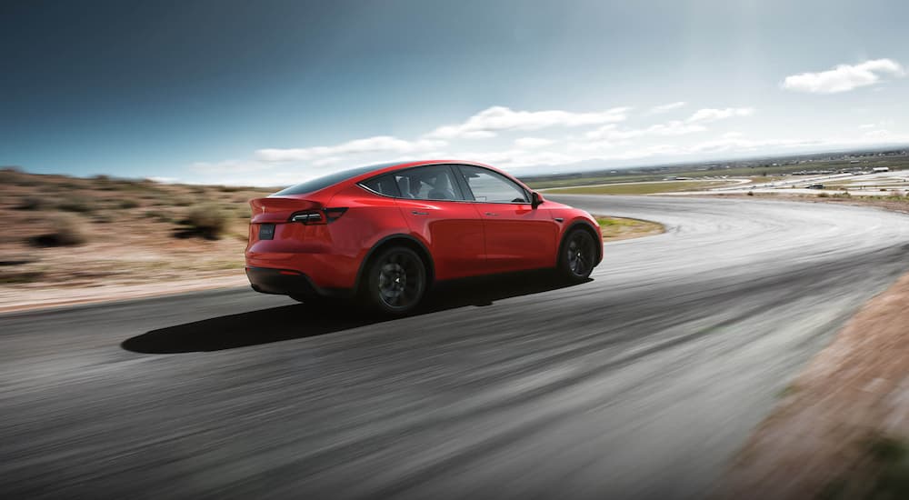 A red 2022 Tesla Model Y is shown from a rear angle driving on an open road.
