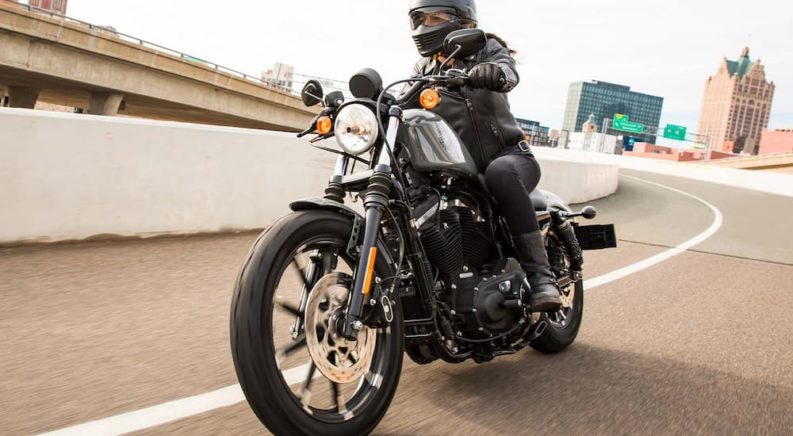A black 2022 Harley-Davidson Iron 883 is shown driving on an open road after leaving a Harley-Davidson dealer.