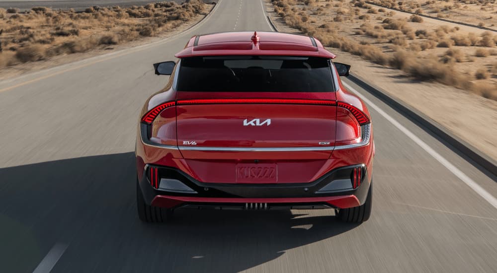 A red 2023 Kia EV6 GT is shown from the rear driving on an open road.