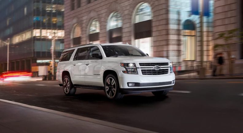 A white 2020 Chevy Suburban is shown driving on a city street after leaving a used Chevy SUV dealer.