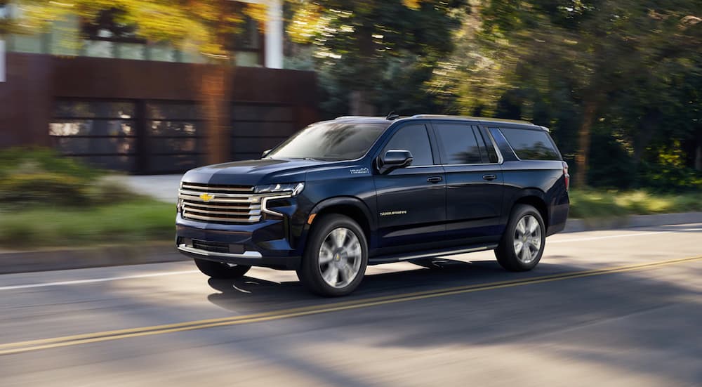 A dark blue 2021 Chevy Suburban High Country is shown from a front angle driving on an open road.