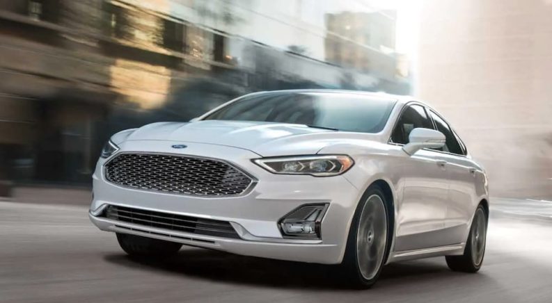 A white 2020 Ford Fusion is shown driving on a city street after leaving a used Ford dealer.