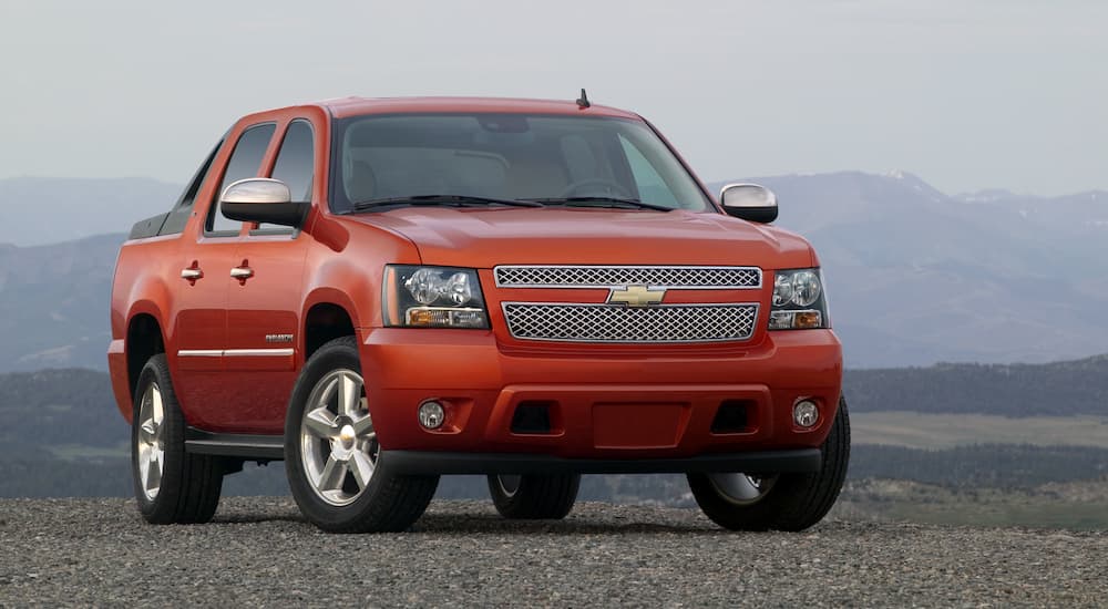 An orange 2010 Chevy Avalanche is shown from the front parked in front of a mountain range.