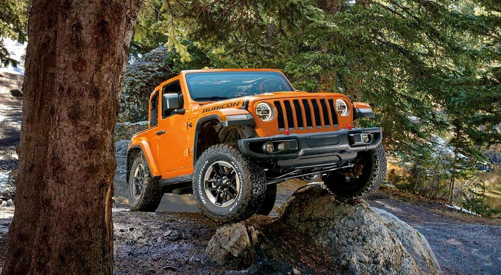 An orange 2023 Jeep Wrangler Rubicon is shown from the front while crawling over a rock.
