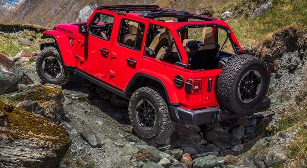A red 2020 Jeep Wrangler Rubicon is shown from the rear at an angle while driving through a rocky area after leaving a dealer that has a Jeep Wrangler Rubicon for sale.